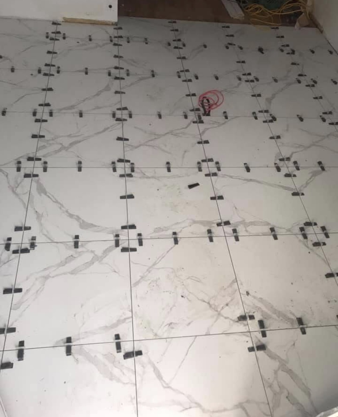 Large-format porcelain marble-look tile installation in progress with leveling clips